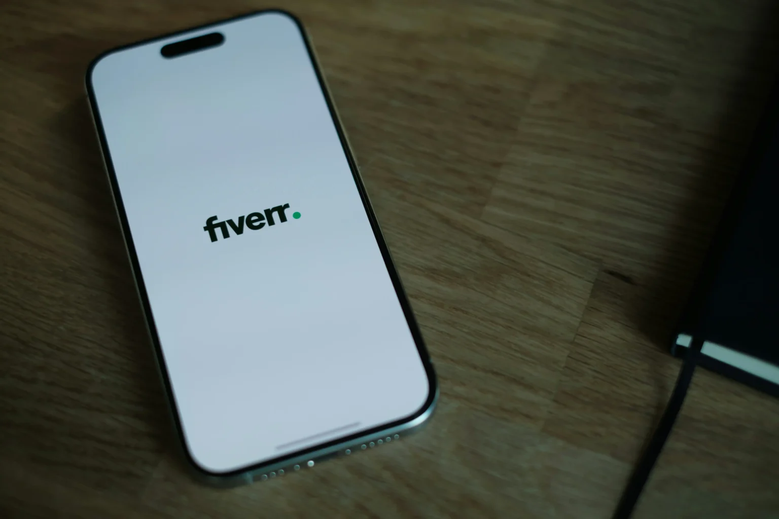 Smartphone displaying Fiverr app logo on screen placed on a wooden desk