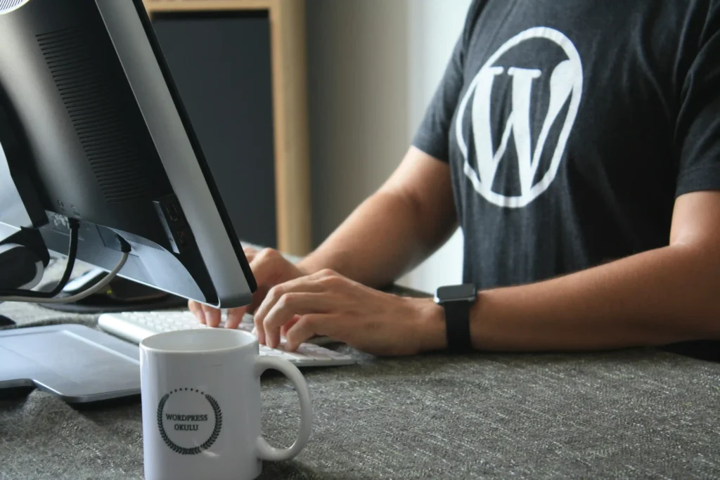 a man working on the laptop wearing black T-shirt on which wordpress white colored logo is printed
