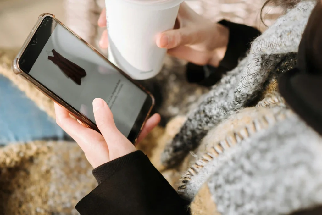 Person browsing clothing product on smartphone while holding a coffee cup